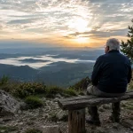 Una persona contempla el paisaje desde un banco de madera mientras reflexiona sobre el camino recorrido y el paso del tiempo.