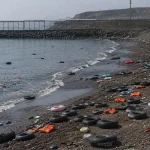Vista del espigón del Tarajal, en Ceuta, con la playa vacía y flotadores abandonados tras una entrada masiva de personas, símbolo de una crisis fronteriza.